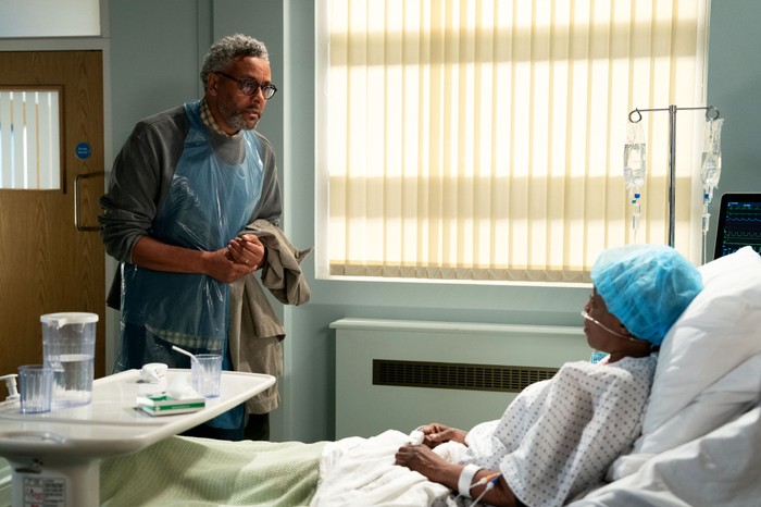 570438,TITLE:Eastenders Darnell stands over Denise, who is in a coma in a hospital bed, in a scene from EastEnders