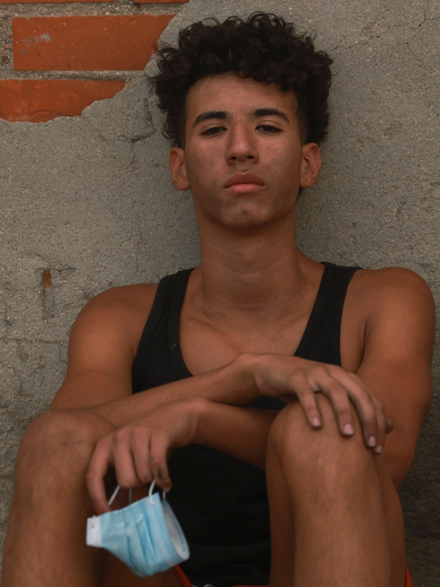 An exhausted young man with black ash across his face sits leaning on a wall.
