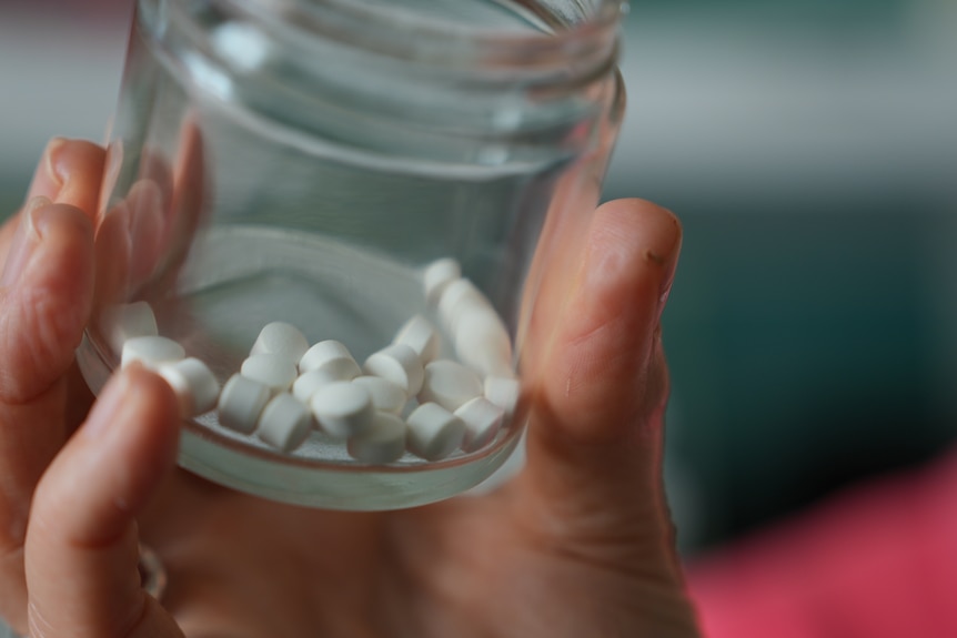 A woman holding a small jar filled with white vitamins.
