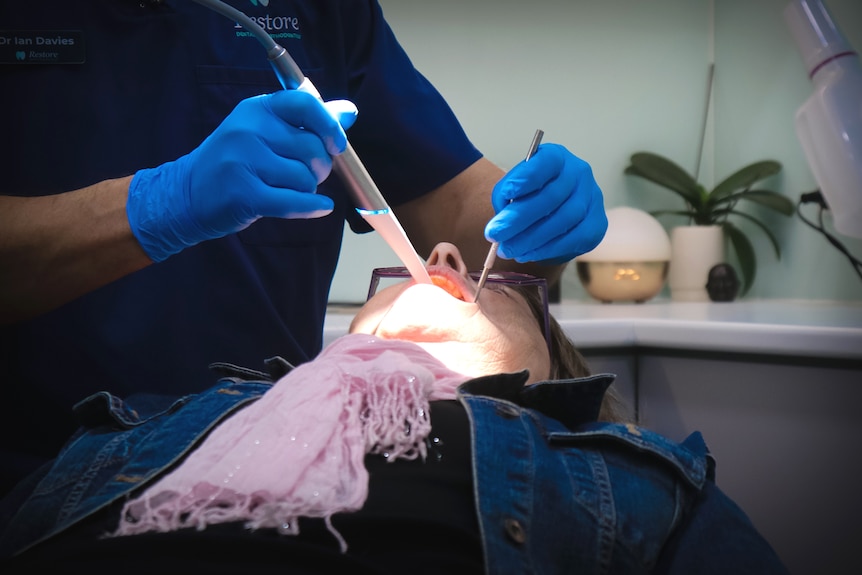 A woman with her mouth open in a dentist's chair while a dentist examines her teeth