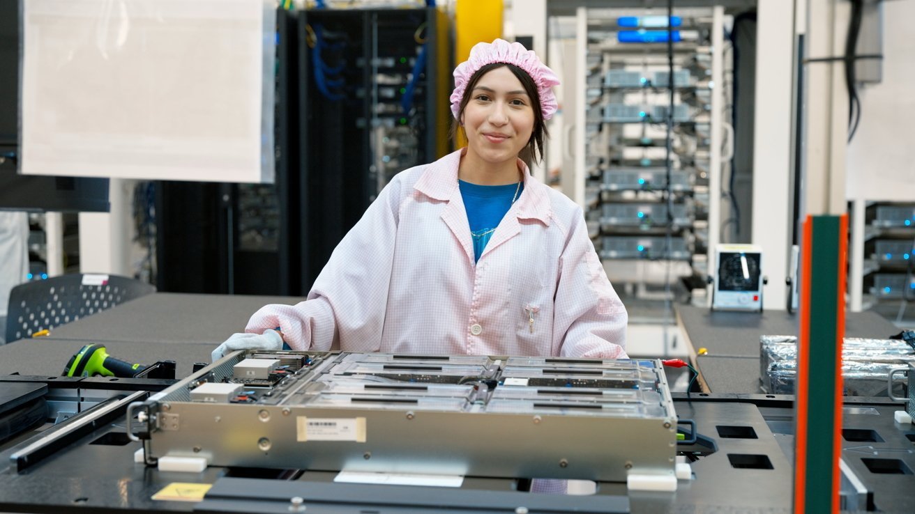Female technician in a pink lab coat and cap working at an electronics assembly station, handling a large circuit board in a clean, modern factory with server racks in the background