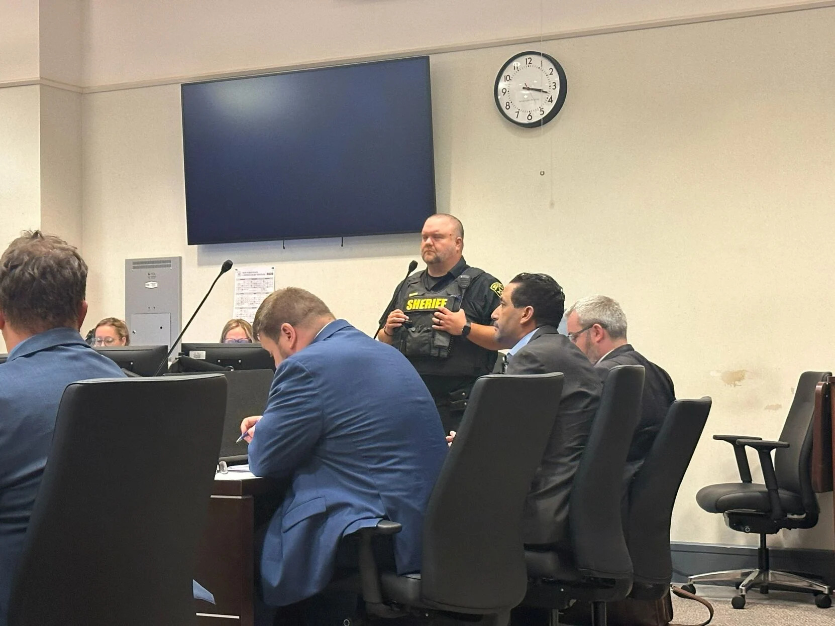 Men in suits sitting around a table while uniformed officer looks on