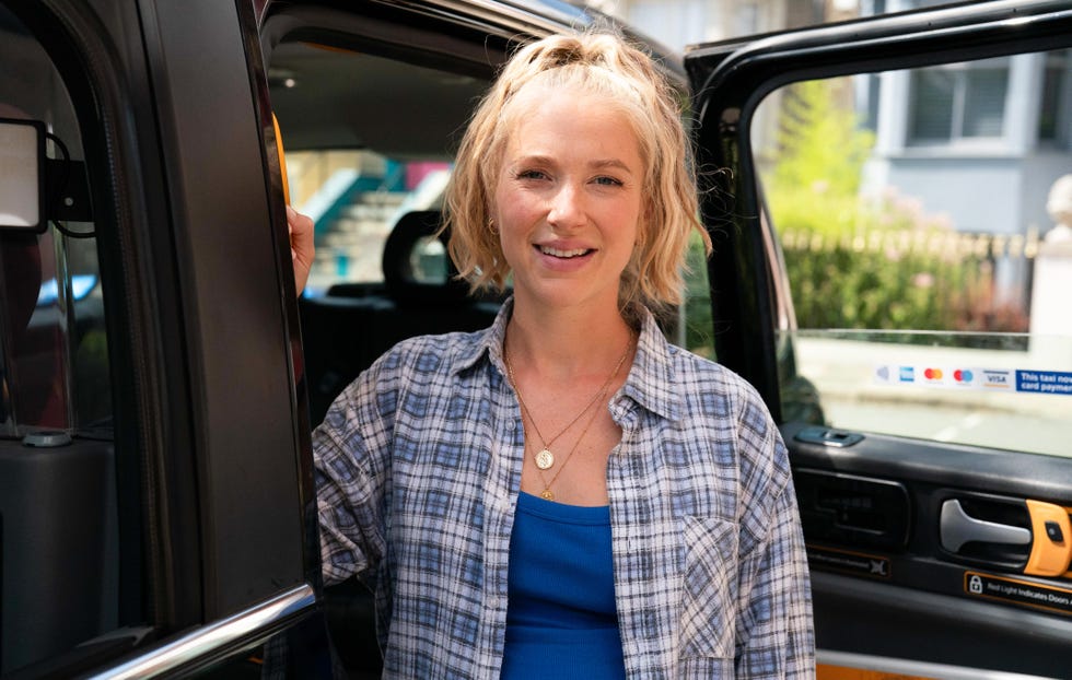 EastEnders, Nancy Carter in 2026 eastenders, maddy hill as nancy carter in 2026, wearing an open blue checkered shirt, standing in front of an open taxi door