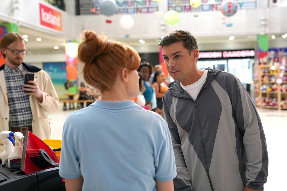 man in gray jacket talking to woman near cleaning cart in mall.
