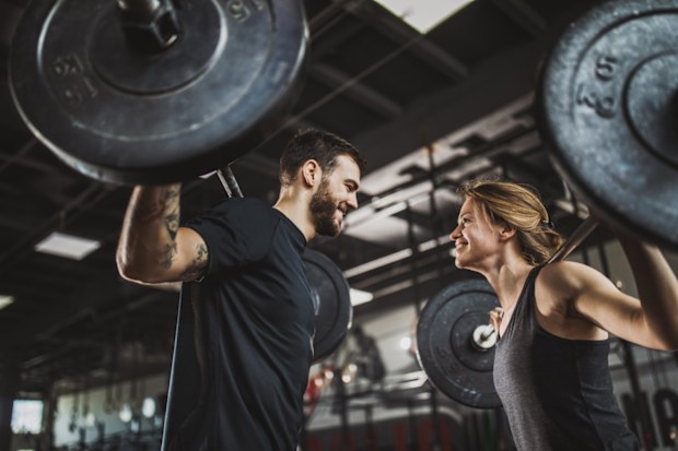 Below view of athletic couple exercising with barbells in a gym.