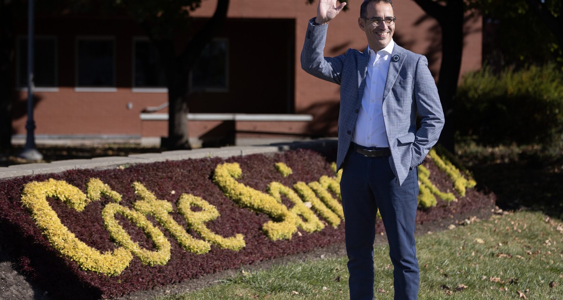 A man waves outside a sign of flowers.