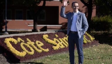 A man waves outside a sign of flowers.