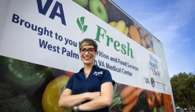 A person stands in front of a truck displaying images of food and signage for VA Fresh and the West Palm Beach VA Medical Center.
