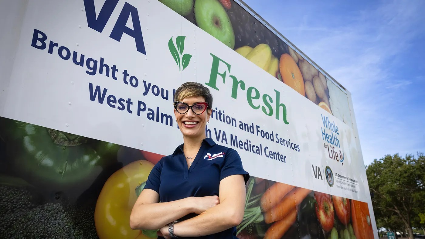 A person stands in front of a truck displaying images of food and signage for VA Fresh and the West Palm Beach VA Medical Center.