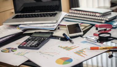 Laptop, calculator and papers scattered across a desk