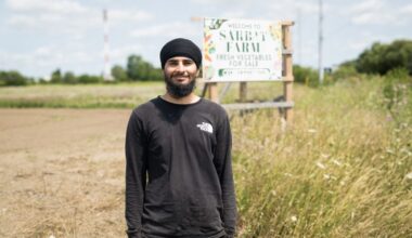 A young man wearing a turban stands in front of a sign that reads Sarbat Farms