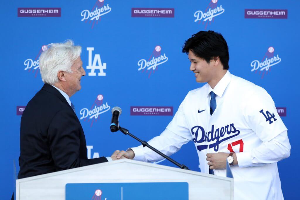 Los Angeles Dodgers owner Mark Walter is shown shaking hands with Shohei Ohtani at an event announcing Ohtani's signing with the team.
