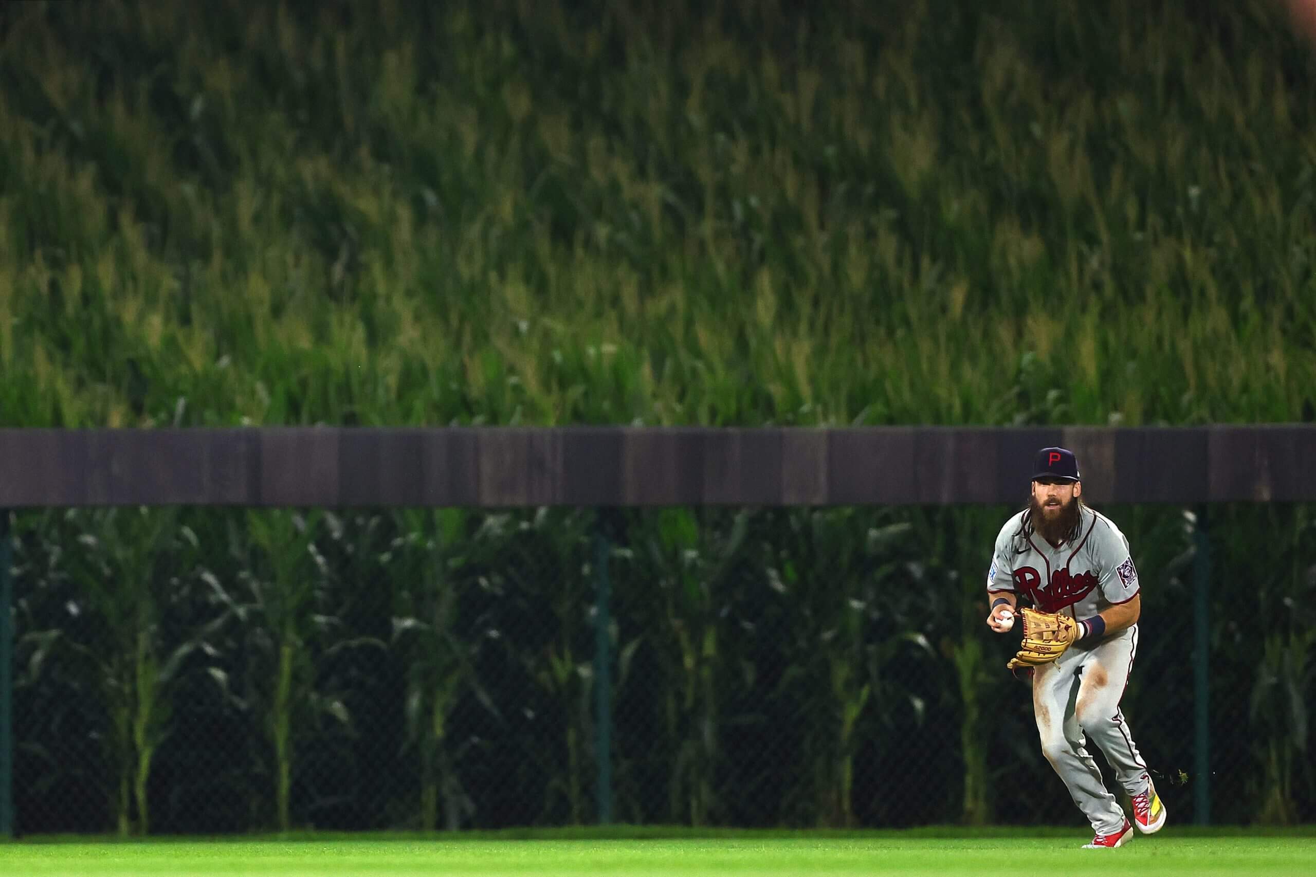 Brandon Marsh bends over with a ball in his right hand and cornstalks in the background.