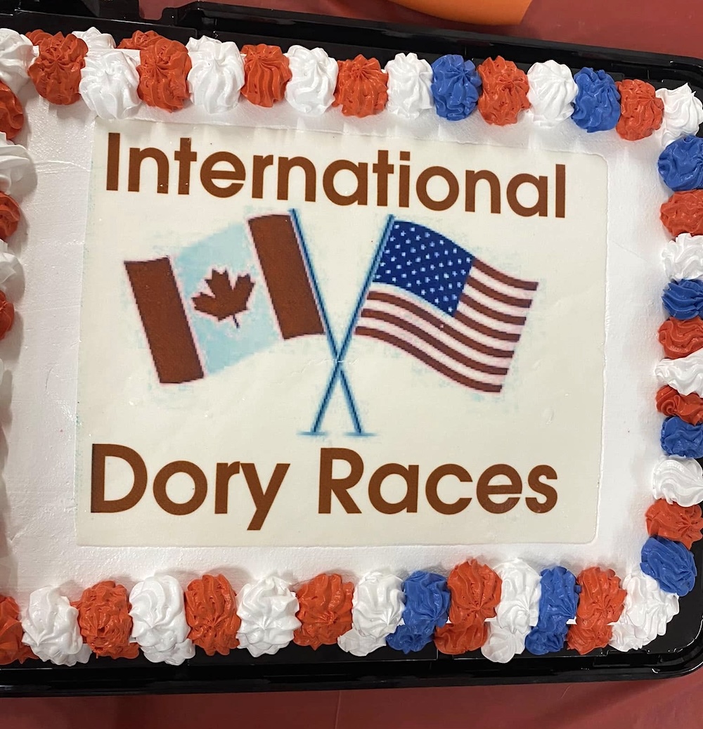 A cake with white icing and the words ‘International Dory Races’ and the U.S. and Canadian flags.