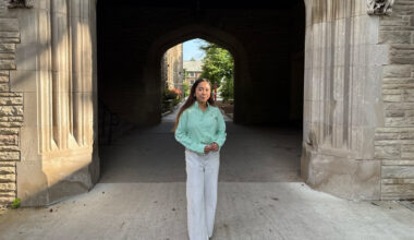 Patricia Mallari, Northeastern master's student, standing beneath a stone archway with a campus building visible through the passage behind her.