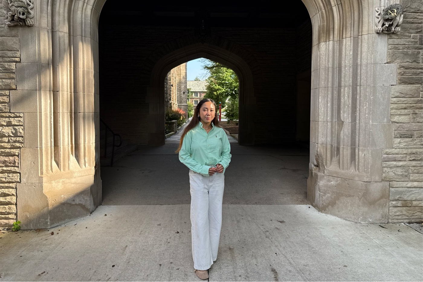 Patricia Mallari, Northeastern master's student, standing beneath a stone archway with a campus building visible through the passage behind her.