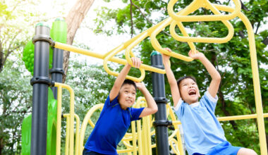 Two kids with medium-light skin tone have fun on the monkey bars.