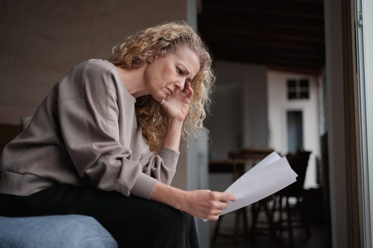 Financial problems. Worried middle-aged woman holding utility bills, managing monthly household budget, sitting on bed feeling anxious. Cost of living concept