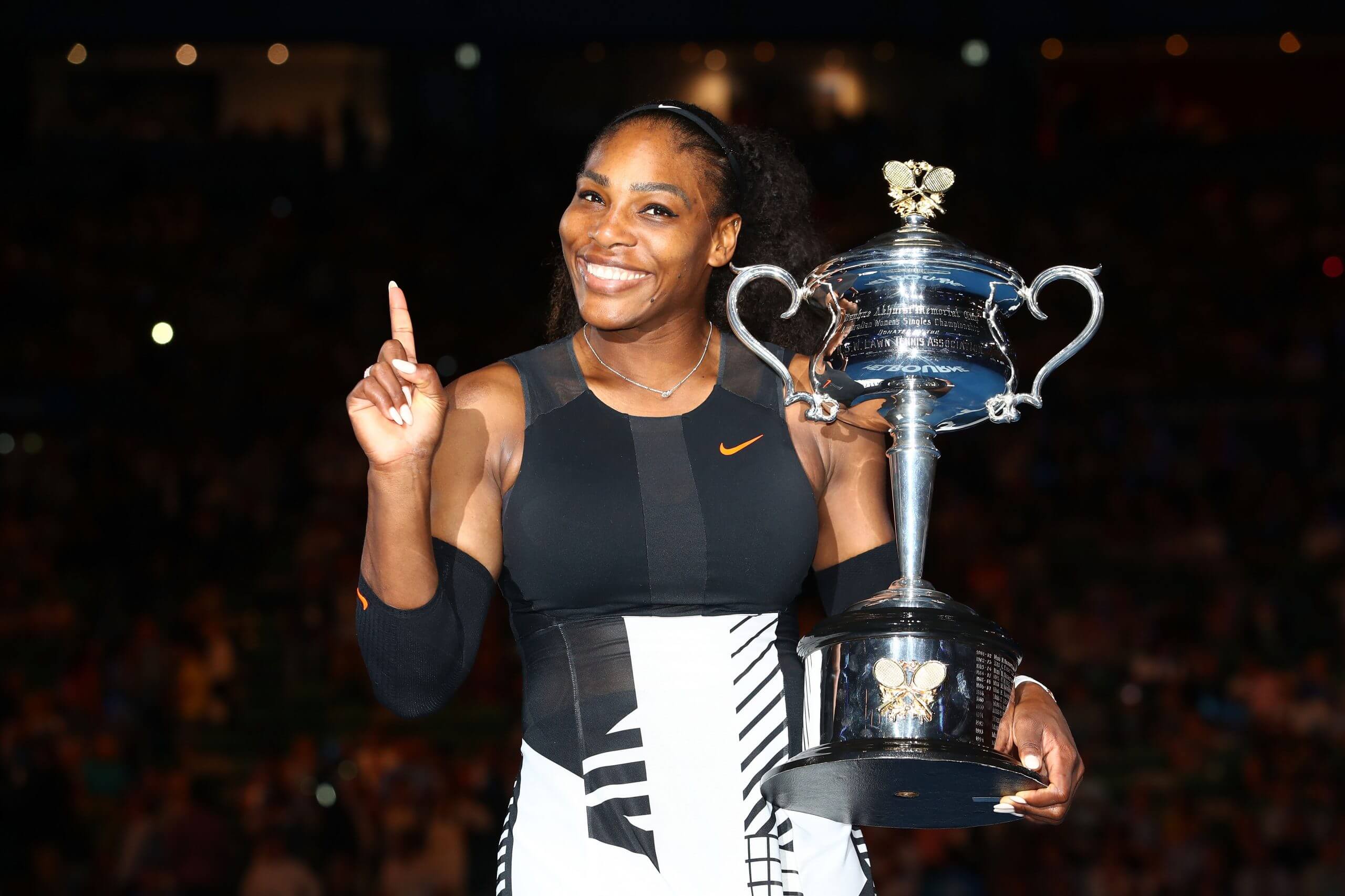 Serena Williams points her index finger on her right hand upward while holding the Austalian Open women's singles trophy.