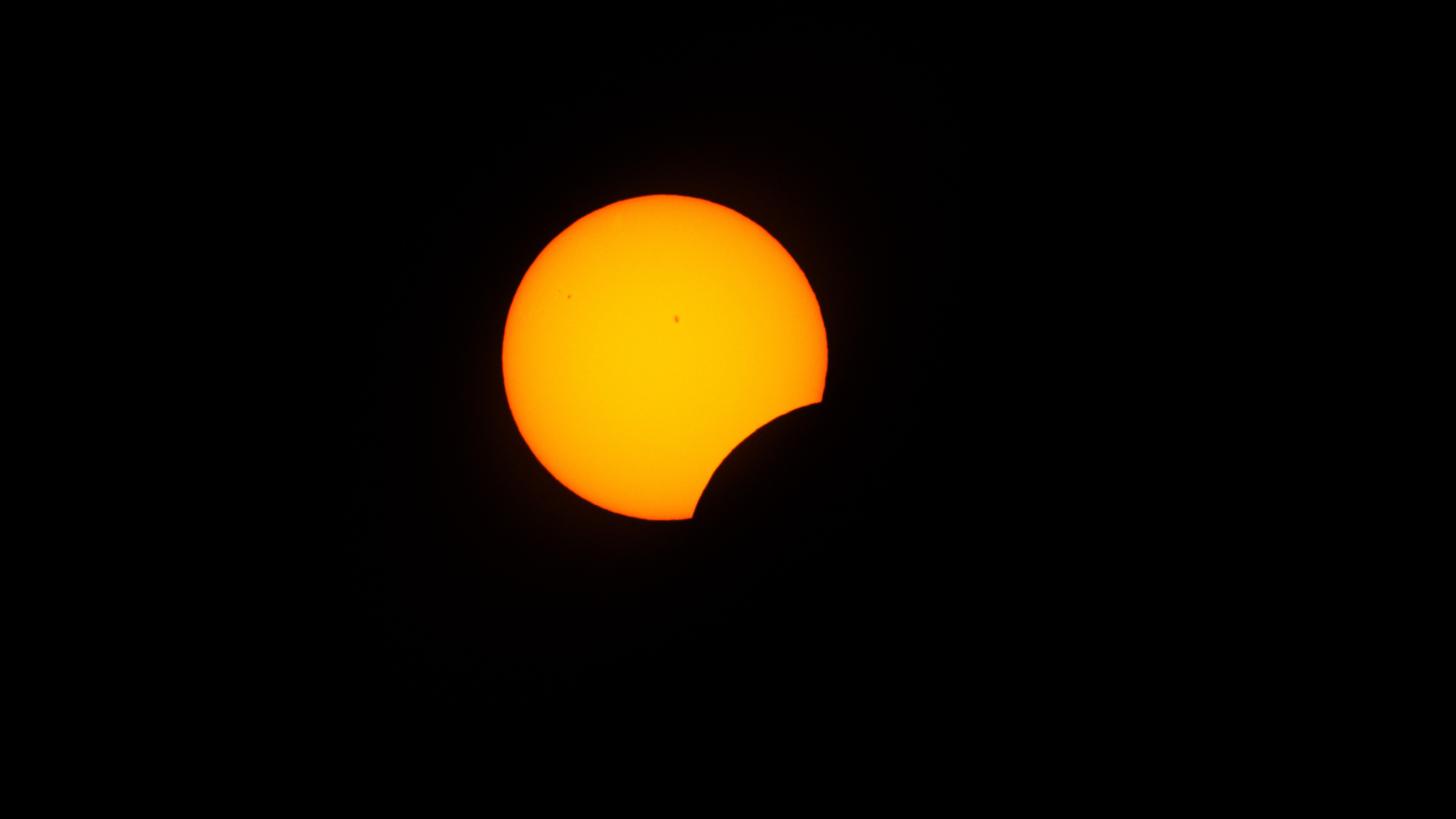 The sun is photographed in a black sky with a part of its lower right disk hidden by the moon's curved silhouette during a solar eclipse.