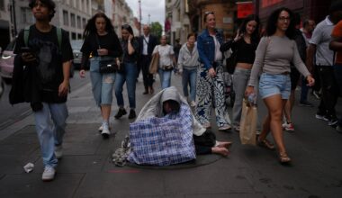 People rush past a man sitting on the street wrapped in a blanket.
