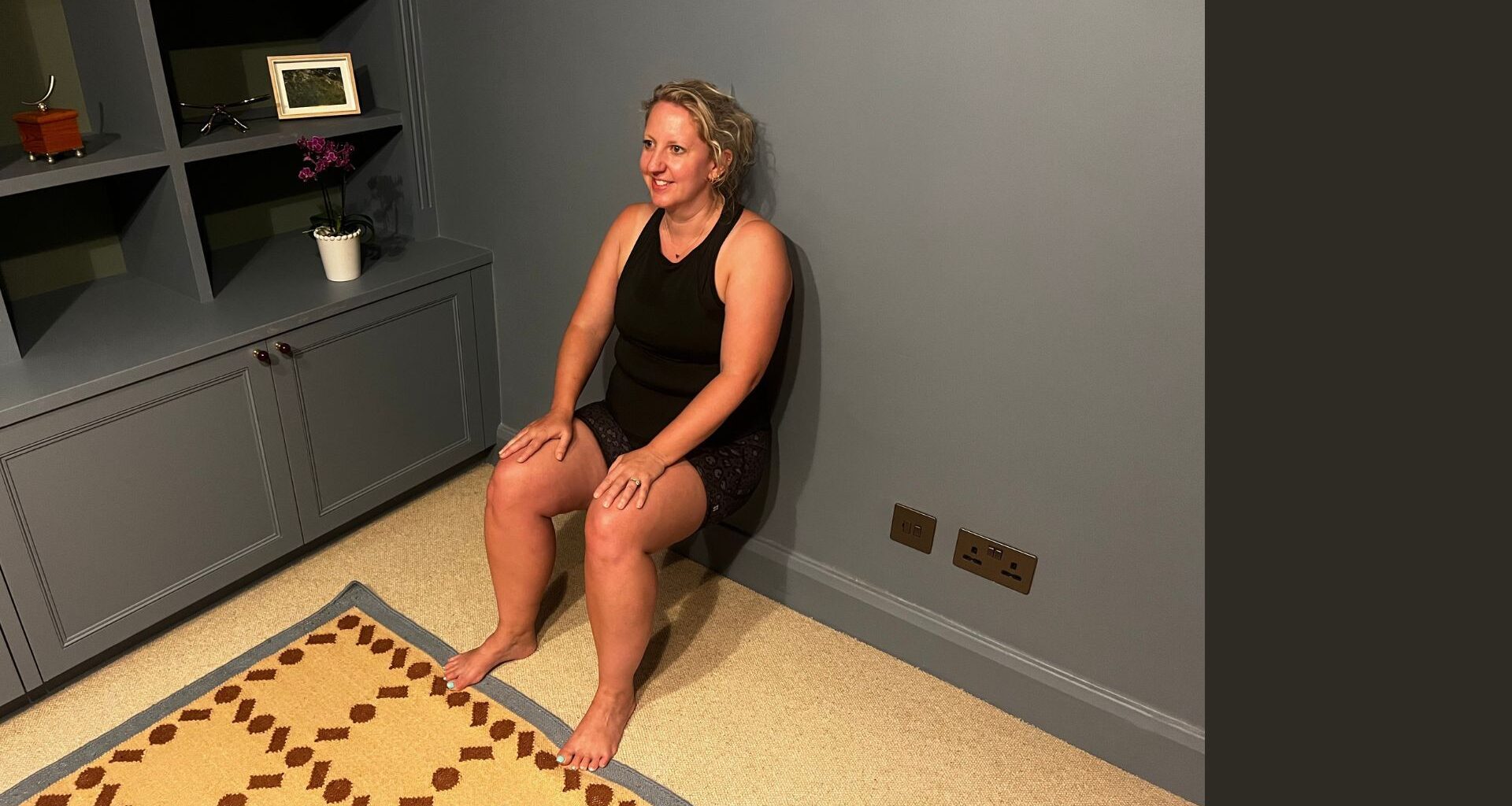 Kat doing wall sit exercise in living room at home
