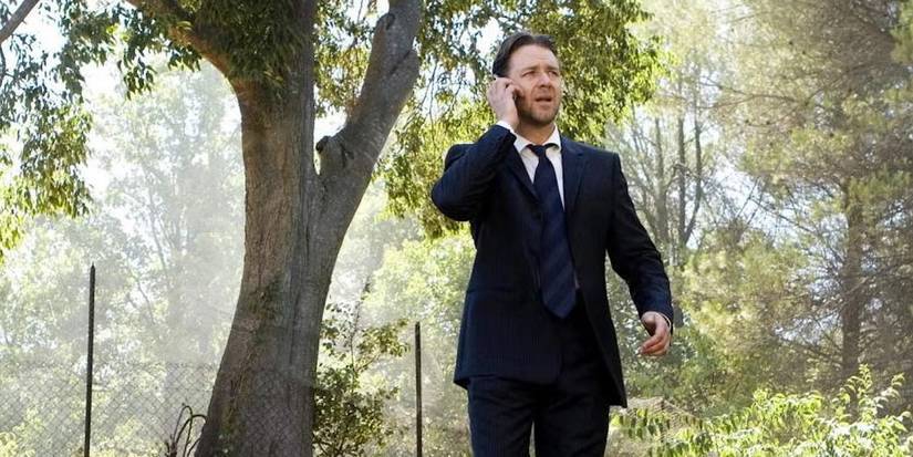 Russell Crowe in a suit and tie talking on a phone outside with trees behind in A Good Year.