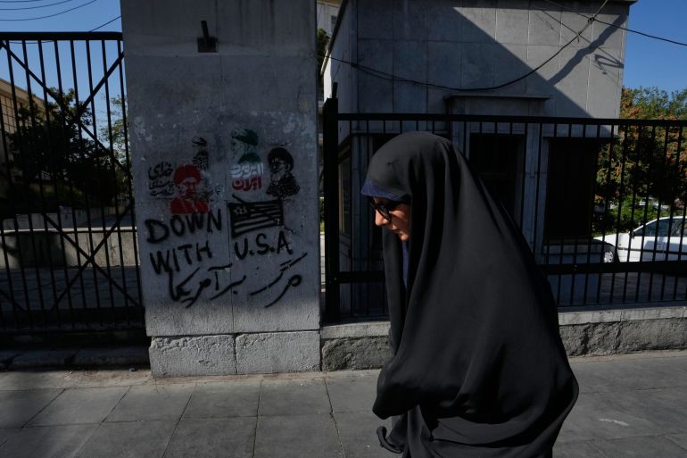 A woman walks past anti-U.S. graffiti and images depicting the late Iranian Supreme Leader Ayatollah Ali Khamenei painted on a wall along Islamic Revolution street in downtown Tehran, Iran, Saturday, Aug. 29, 2026. (AP Photo/Vahid Salemi)