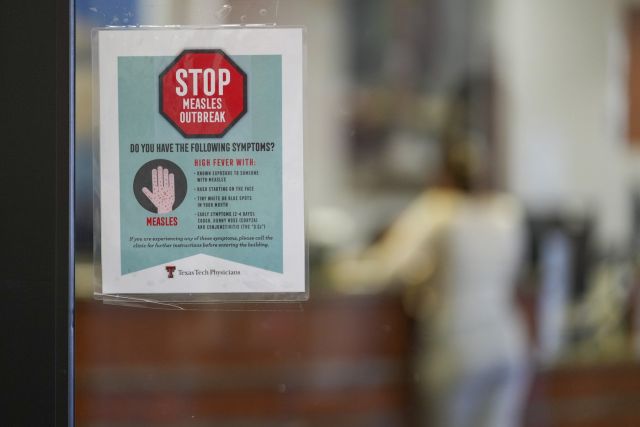 A sign warning of measles is posted on a glass door as a patient checks in for an appointment in the family medicine wing of at the Texas Tech Physicians of the Permian Basin Monday, Feb. 24, 2025, in Odessa, Texas. (AP Photo/Julio Cortez)
