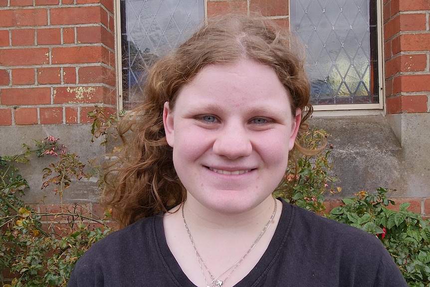 teenage girl looks to camera and smiles. She had curly, light brown hair pulled back.