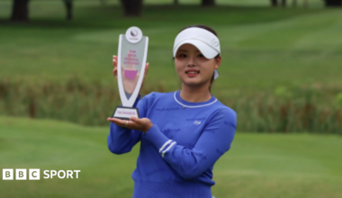 Jessica Bang posing for photographs on a golf course while holding a trophy