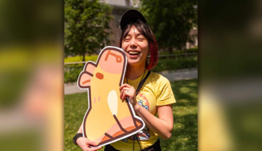 A woman is smiling, holding a cardboard cutout of a capybara