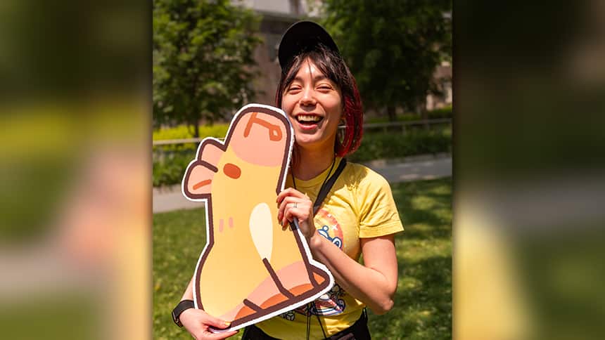 A woman is smiling, holding a cardboard cutout of a capybara