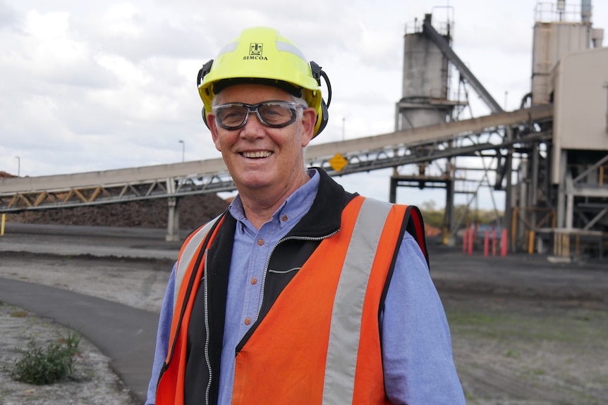 A smiling man in a hard hat and high-vis on an industrial site.