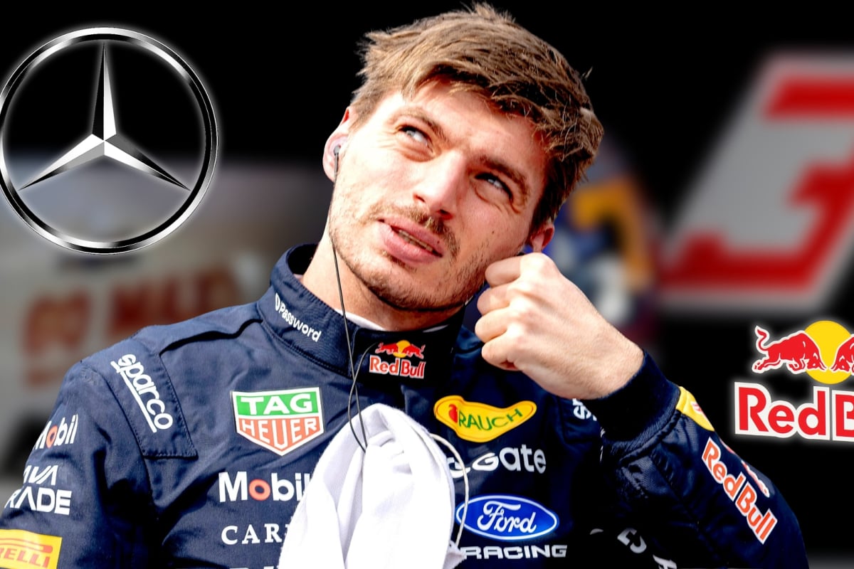 Verstappen in Red Bull race suit looking at Mercedes logo with blurred background of Red Bull garage and No.3