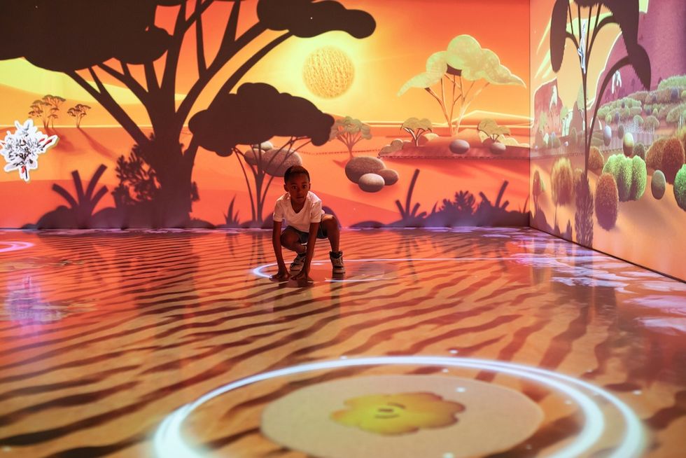 Child crouches on colorful interactive floor in sunset-themed room, Geoverse \u201cA Day in the Desert"