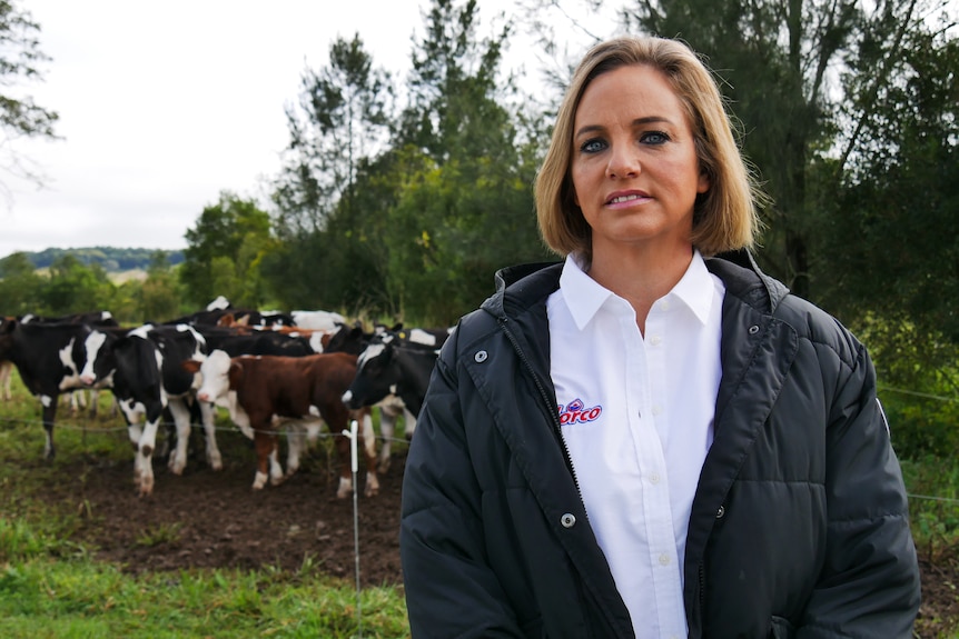 Jane Polson standing in front of a wire fence, with a herd of cows gathering just behind.