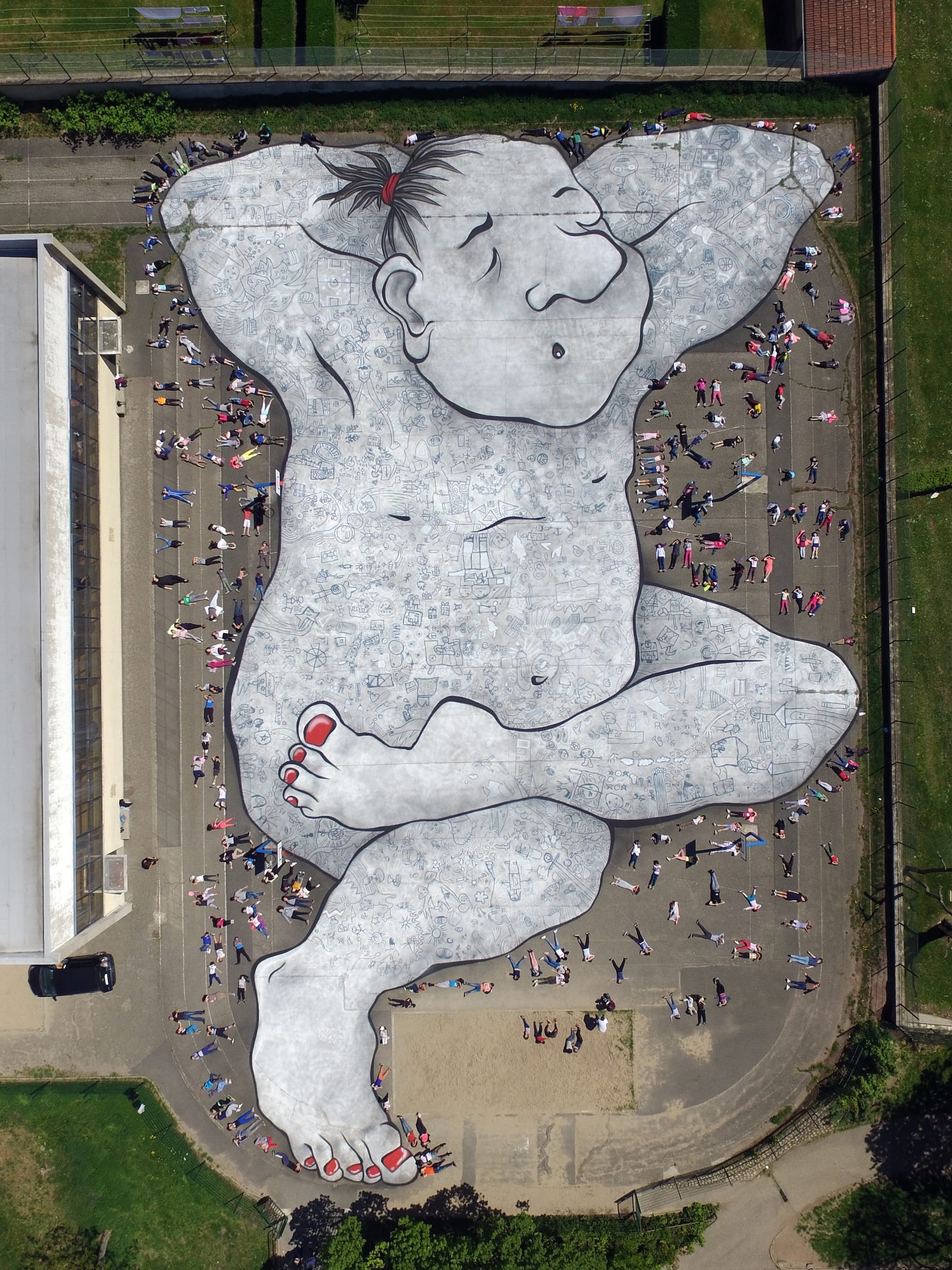 an aerial view of a large mural by Ella & Pitr on the ground of a public square featuring a cartoonish sleeping figure