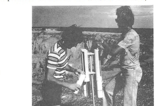 An old black-and-white photo of two men outdoors, standing by an instrument consisting of vertical tubes.