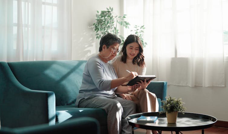 An older woman and a younger woman look at a computer screen together while sitting on a couch.