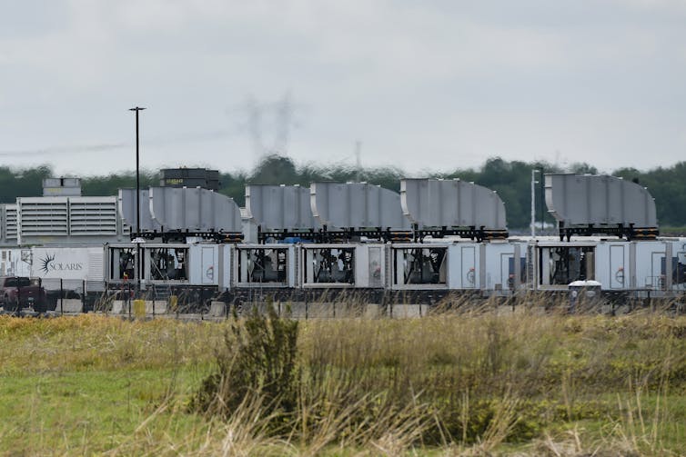 A view across a grassy area of large metal industrial boxes.