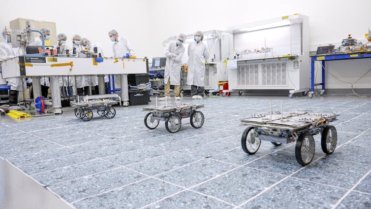 Three small robotic rovers drive across a sterile warehouse floor.