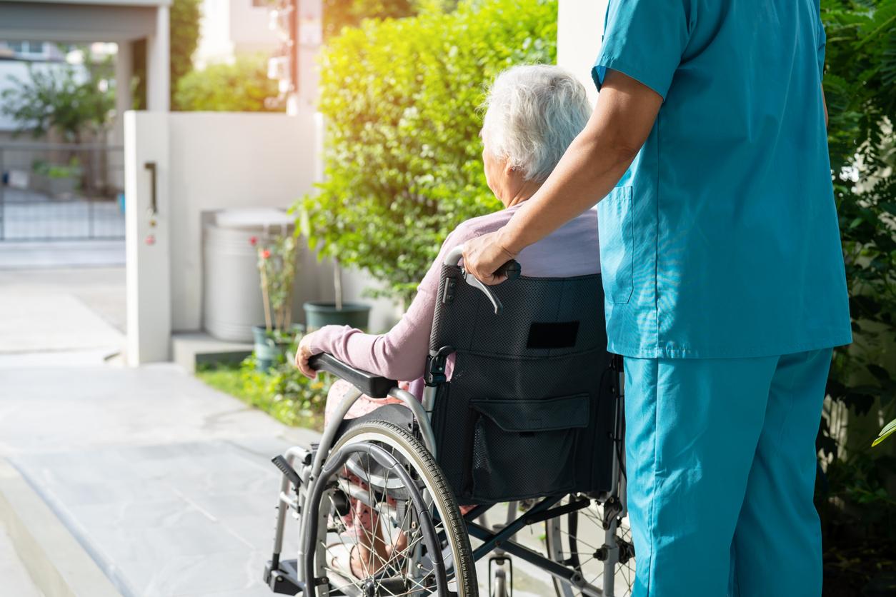 Nursing home attendant in blue scrubs pushing female resident in wheelchair