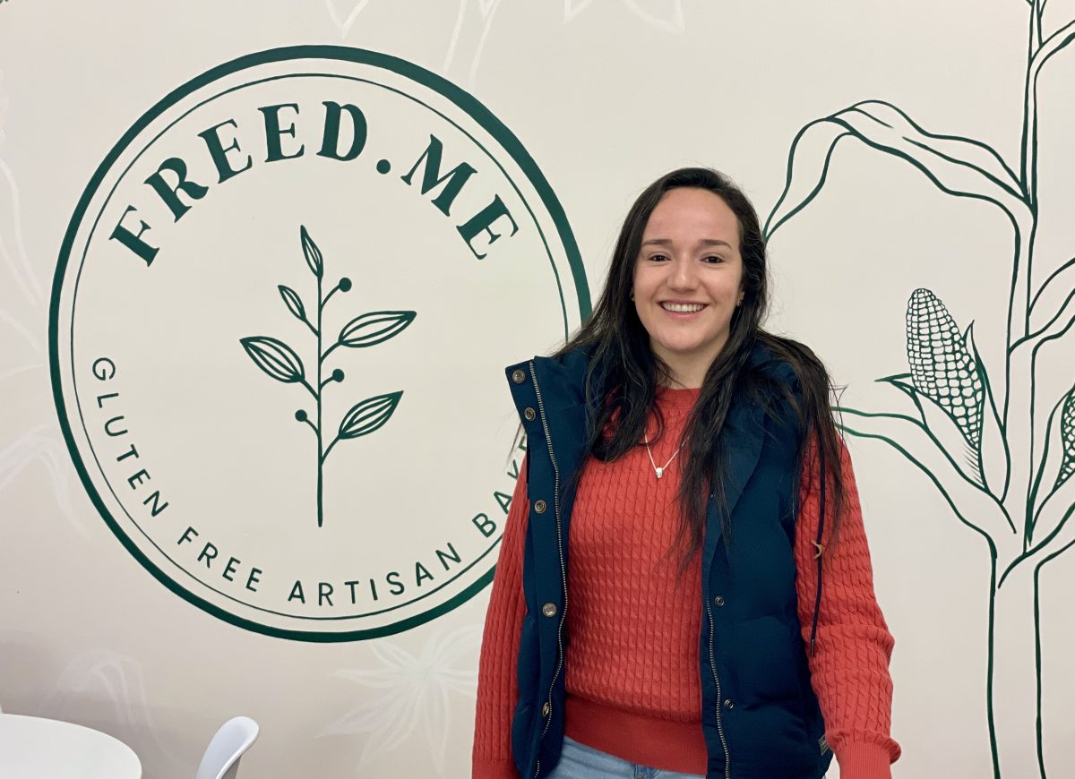A young Colombian woman wears a red jumper and blue vest, and stands in front of the Freed.me logo.