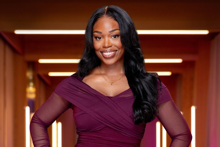 Chevanique smiling ahead, wearing a purple dress with her hands on her hips.]