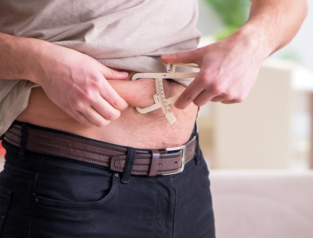 Man measuring body fat with calipers on his abdomen.