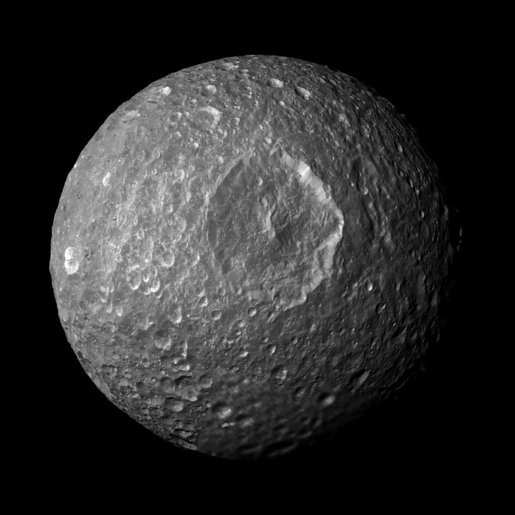 Mimas looks like one of Saturn's deadest moons: a frozen, heavily cratered ball with no obvious activity. Then scientists discovered a global ocean beneath it in 2024 — an ocean less than 25 million years old, younger than the Himalayas, hiding beneath a surface that gives almost nothing away.