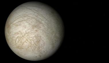 Europa is smaller than Earth's Moon, yet the ocean locked beneath its ice contains more liquid water than every ocean on Earth combined — kept from freezing not by sunlight, but by Jupiter's gravity squeezing the moon like a slow, endless fist