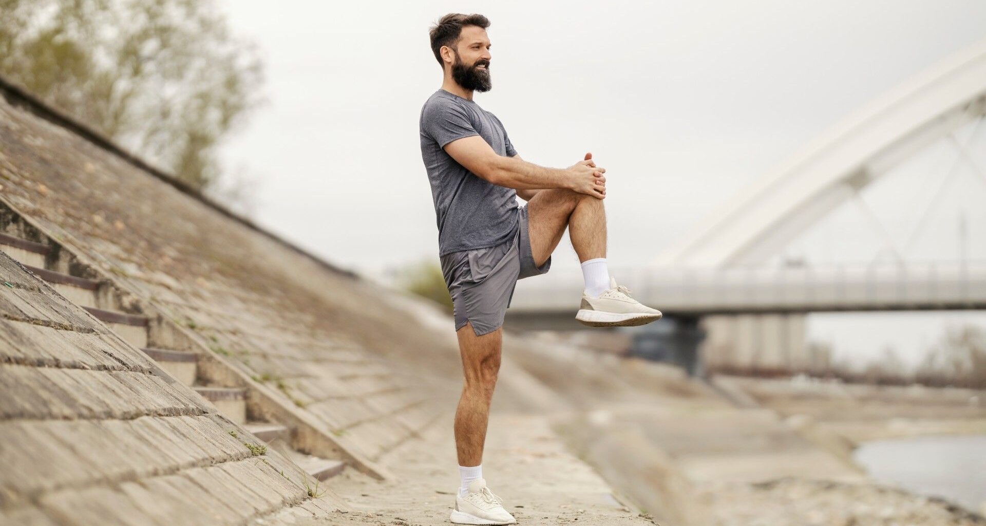 Male in shorts and t-shirt balancing on one leg while hugging his knee outdoors