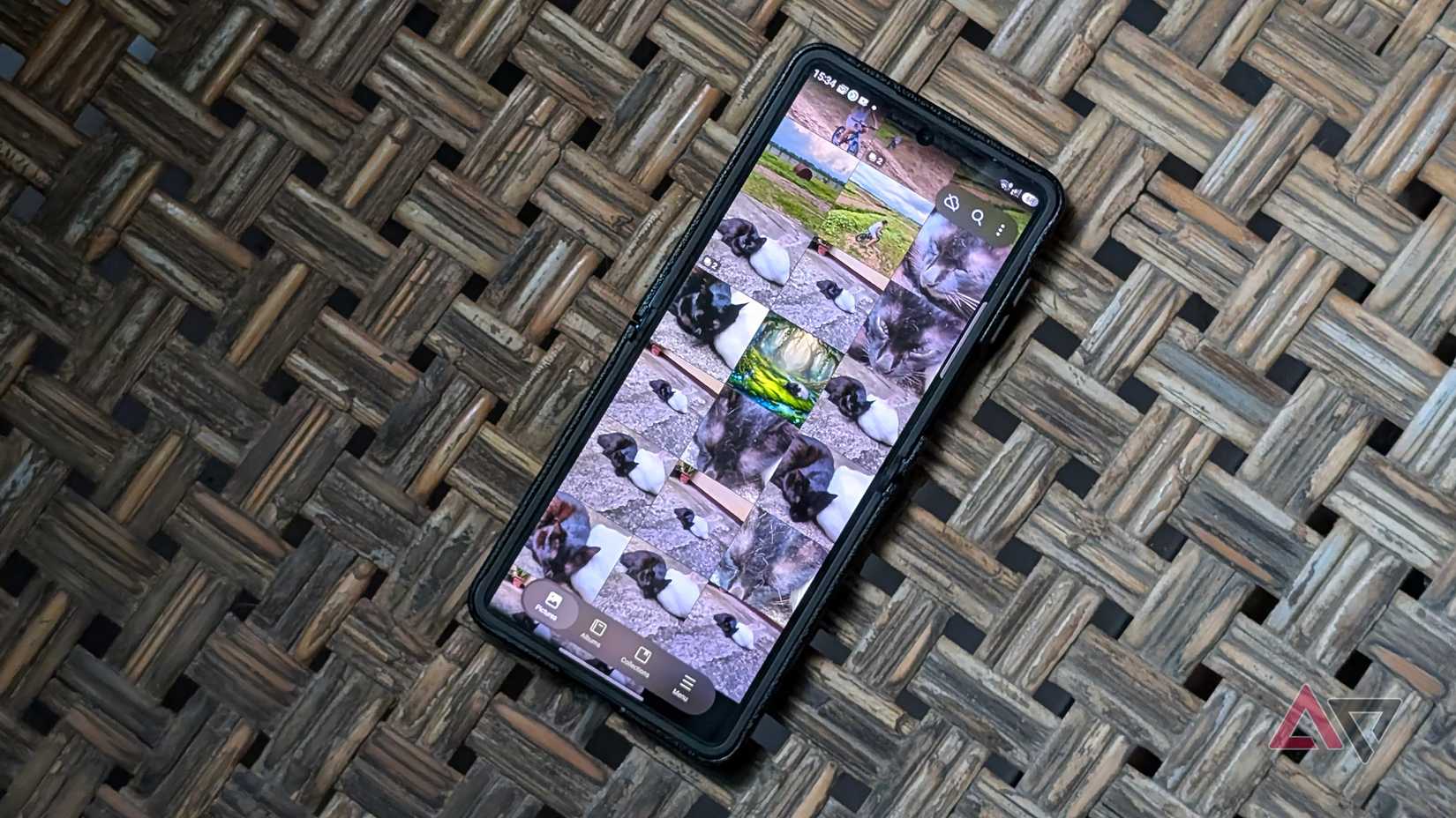A Samsung Galaxy Z Flip 7 smartphone on a woven chair with its screen showing the gallery app with cat pictures
